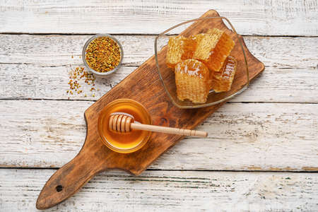 Bowls of honey, combs and bee pollen on white wooden backgroundの写真素材