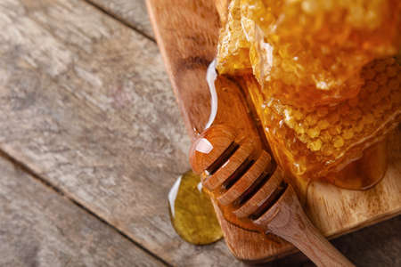 Board with honey combs and dipper on wooden background, closeup