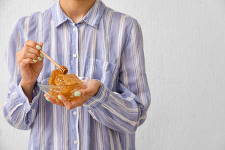 Woman holding bowl of honey combs with dipper on light background, closeupの写真素材