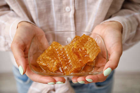 Woman holding bowl of honey combs on light backgroundの写真素材