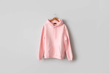 Stylish pink hoodie hanging on light wall