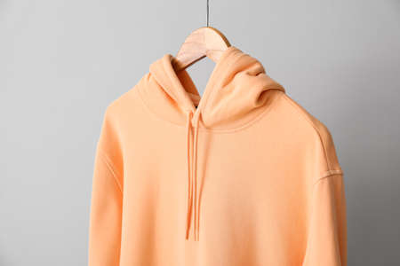 Stylish peachy hoodie near light wall, closeup