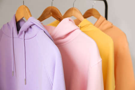 Rack with stylish hoodies near light wall, closeup