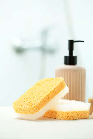 Bath sponges and bottle of cosmetic product on table in bathroom, closeup