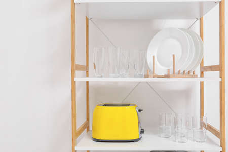Shelving unit with glasses, plates and toaster near light wall