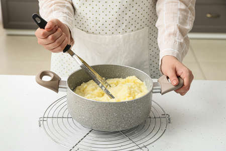 Woman preparing tasty mashed potatoes on table in kitchen, closeupの写真素材