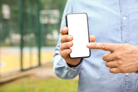 Man holding mobile phone and pointing on blank screen outdoors, closeup