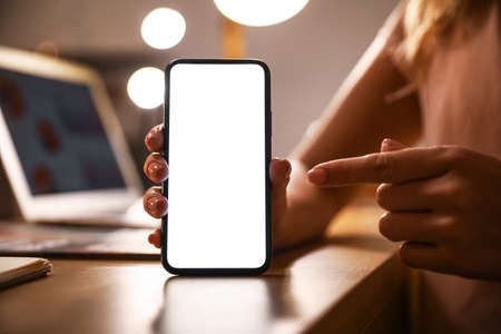 Woman pointing on blank mobile phone screen in office, closeup