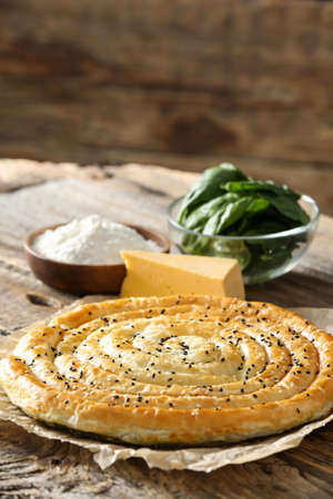Tasty spinach pie and ingredients on wooden backgroundの写真素材