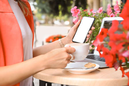 Young woman holding mobile phone and drinking cappuccino in cafe, closeupの写真素材