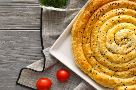 Plate with tasty spinach pie on gray wooden background, closeup