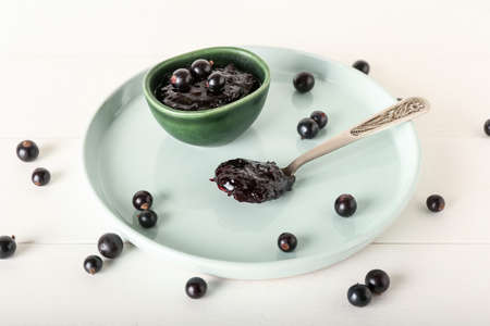Bowl and spoon with black currant jam on light wooden backgroundの写真素材