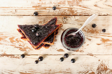 Jar and toasts with black currant jam on light wooden backgroundの写真素材