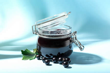 Jar with black currant jam on color background