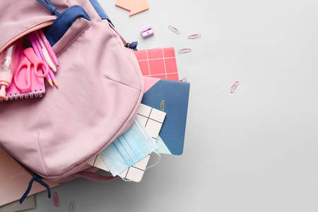 School backpack and stationery on light background