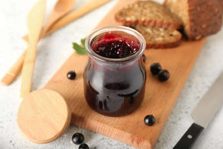 Wooden board with delicious black currant jam in jar on light backgroundの写真素材