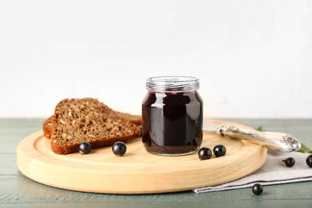 Jar with delicious black currant jam and bread on color wooden tableの写真素材