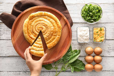 Woman taking slice of spinach pie on light wooden backgroundの写真素材
