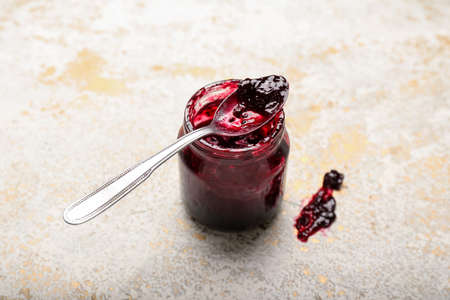 Delicious black currant jam in jar and spoon on light backgroundの写真素材
