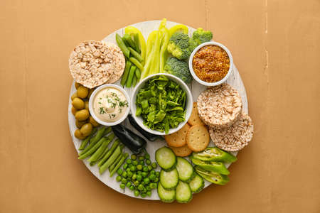 Wooden board with different green vegetables and bowls with sauce on color backgroundの写真素材