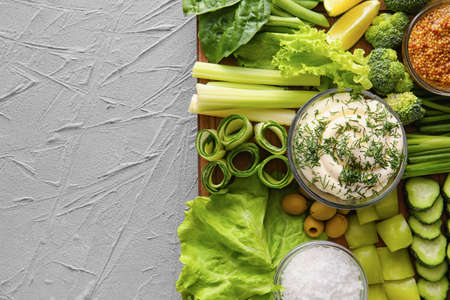 Wooden board with different green vegetables and bowl with sauce on gray background, closeupの写真素材