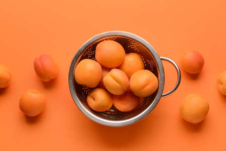 Colander with tasty ripe apricots on color background