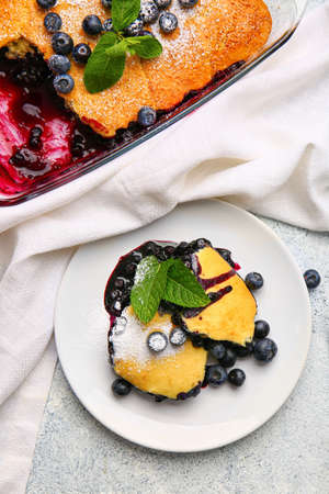 Plate with pieces of blueberry cobbler on light background