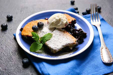 Plate with pieces of blueberry cobbler and ice cream on dark background, closeup
