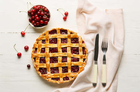 Tasty cherry pie and cutlery on light wooden background