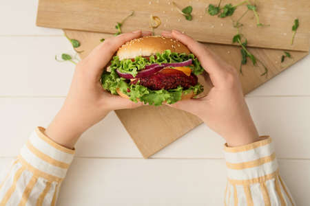 Woman holding tasty vegetarian burger on white wooden backgroundの写真素材