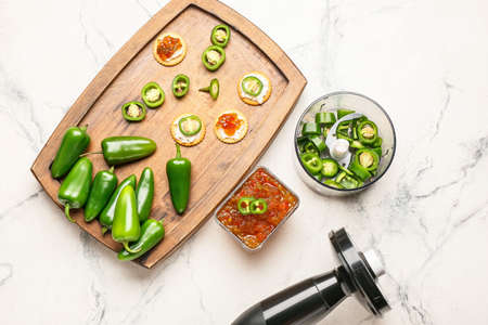 Bowl with delicious jalapeno pepper jam and wooden board with crackers on light tableの写真素材