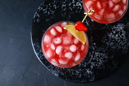 Glasses of tasty strawberry margarita on dark background, closeup