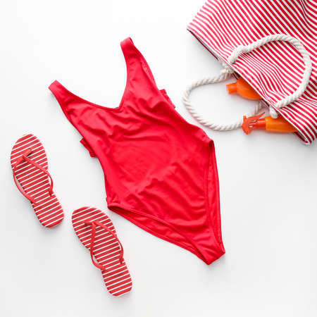 Stylish swimsuit, flip-flops and bag with sunscreen cream on white background