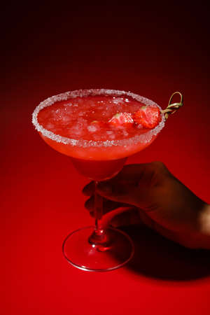 Woman holding glass of tasty strawberry margarita on color backgroundの写真素材