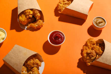 Paper boxes with tasty popcorn chicken and sauces on color backgroundの写真素材