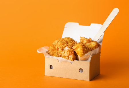 Paper box with tasty fried popcorn chicken on color backgroundの写真素材