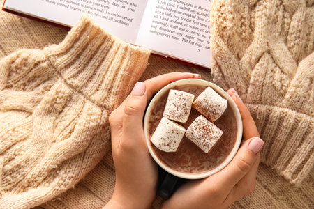 Female hands with cup of cacao, sweater and book, closeupの写真素材