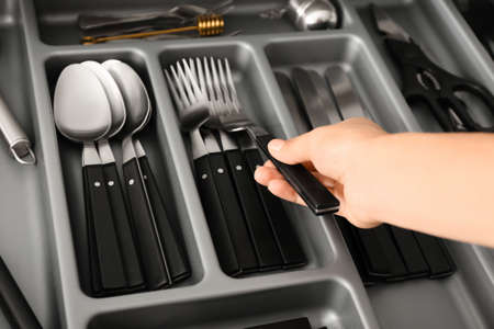 Woman putting clean fork into kitchen drawer, closeup