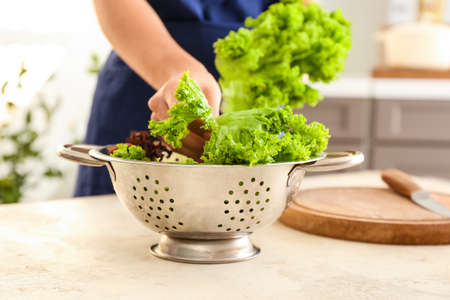 Woman putting lettuce leaves into colander in kitchen, closeupの写真素材