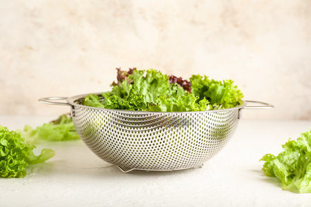 Colander with fresh lettuce on light background