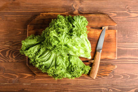 Board with fresh lettuce and knife on wooden background