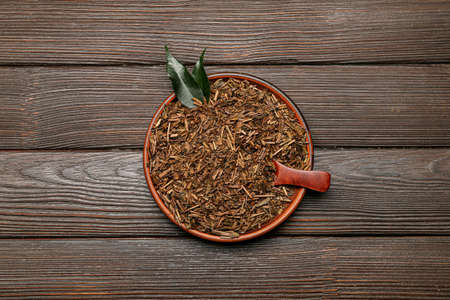 Plate with dry hojicha green tea on dark wooden background