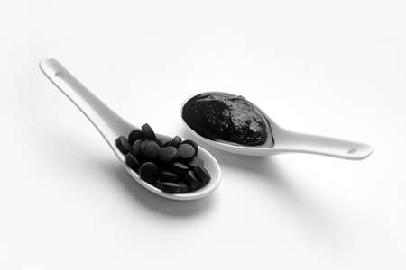 Spoons with activated carbon mask and pills on white background