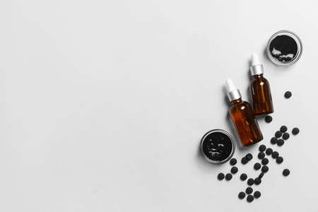 Bowls with activated carbon mask, pills and bottles of essential oil on white backgroundの写真素材