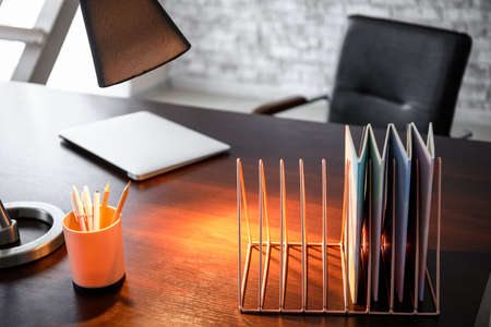Metal organizer with notebooks, stationery and glowing lamp on table in officeの写真素材