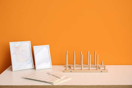 Wooden organizer with notebooks and frames on shelf near orange wall