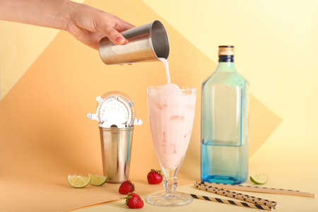 Woman pouring strawberry Pina Colada cocktail into glass on color background