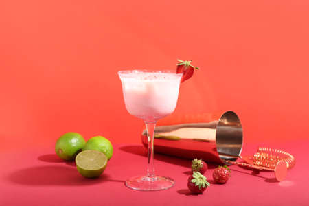 Composition with glass of strawberry Pina Colada cocktail, limes, berries and shaker on color...