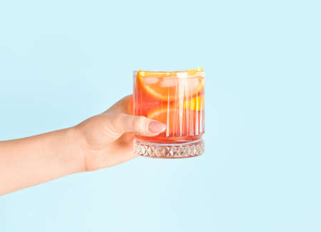 Woman holding glass of tasty Negroni cocktail on color background, closeup
