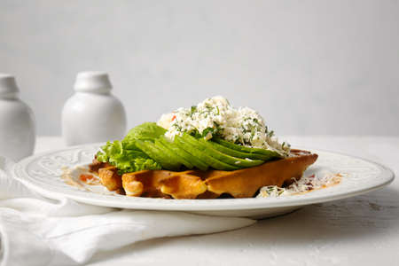 Delicious Belgian waffle with egg, avocado and cheese in plate on table, closeup